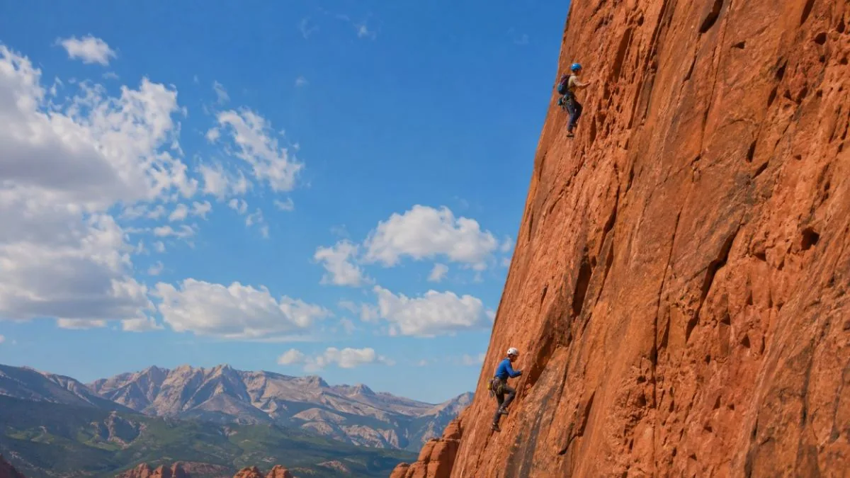 Two roped rock climbers on a steep red sandstone face