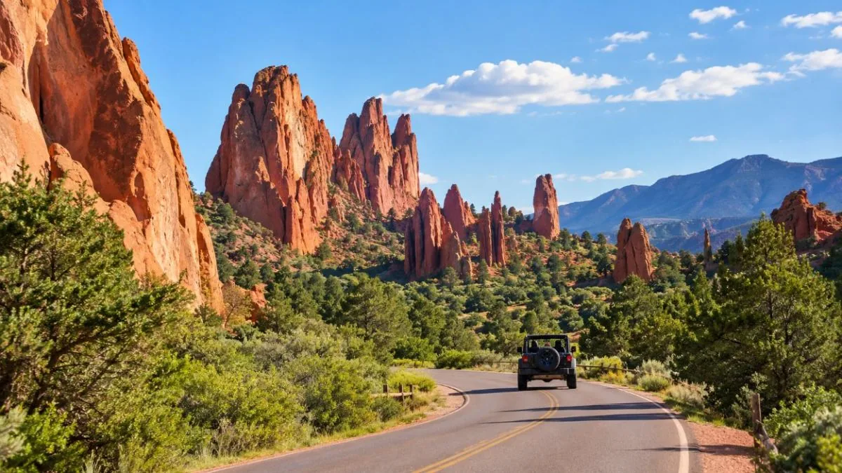 An open-air jeep on a park road below red sandstone formations