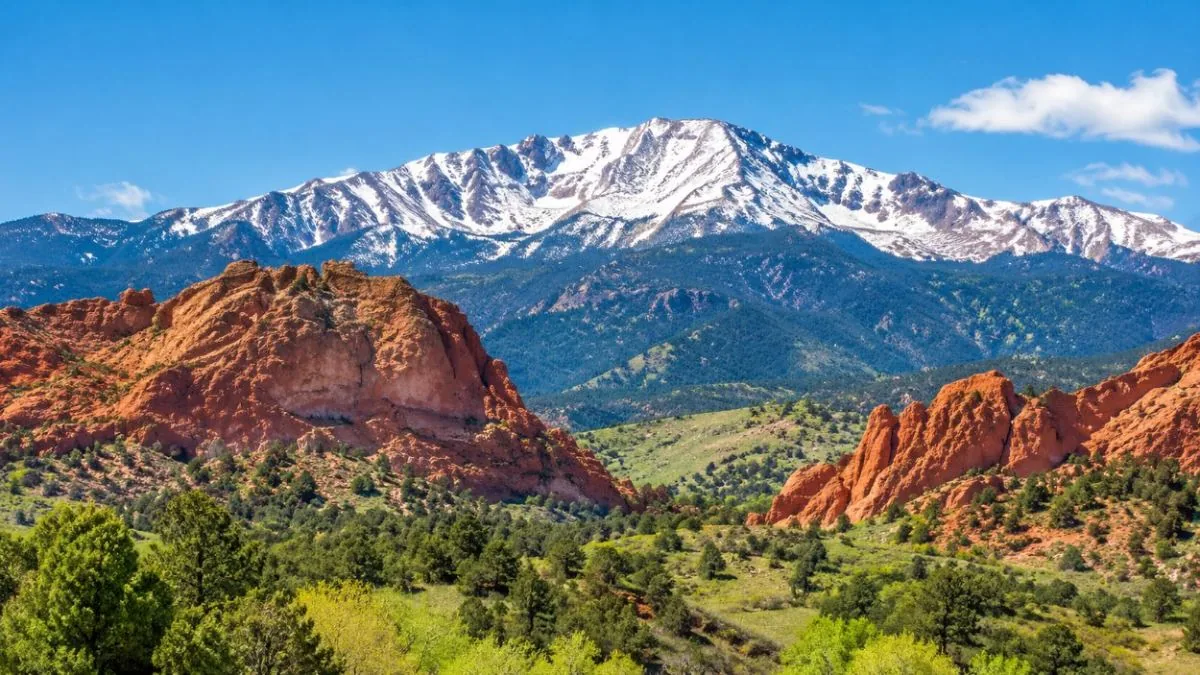 Snow-capped Pikes Peak rising behind red rocks and green foothills